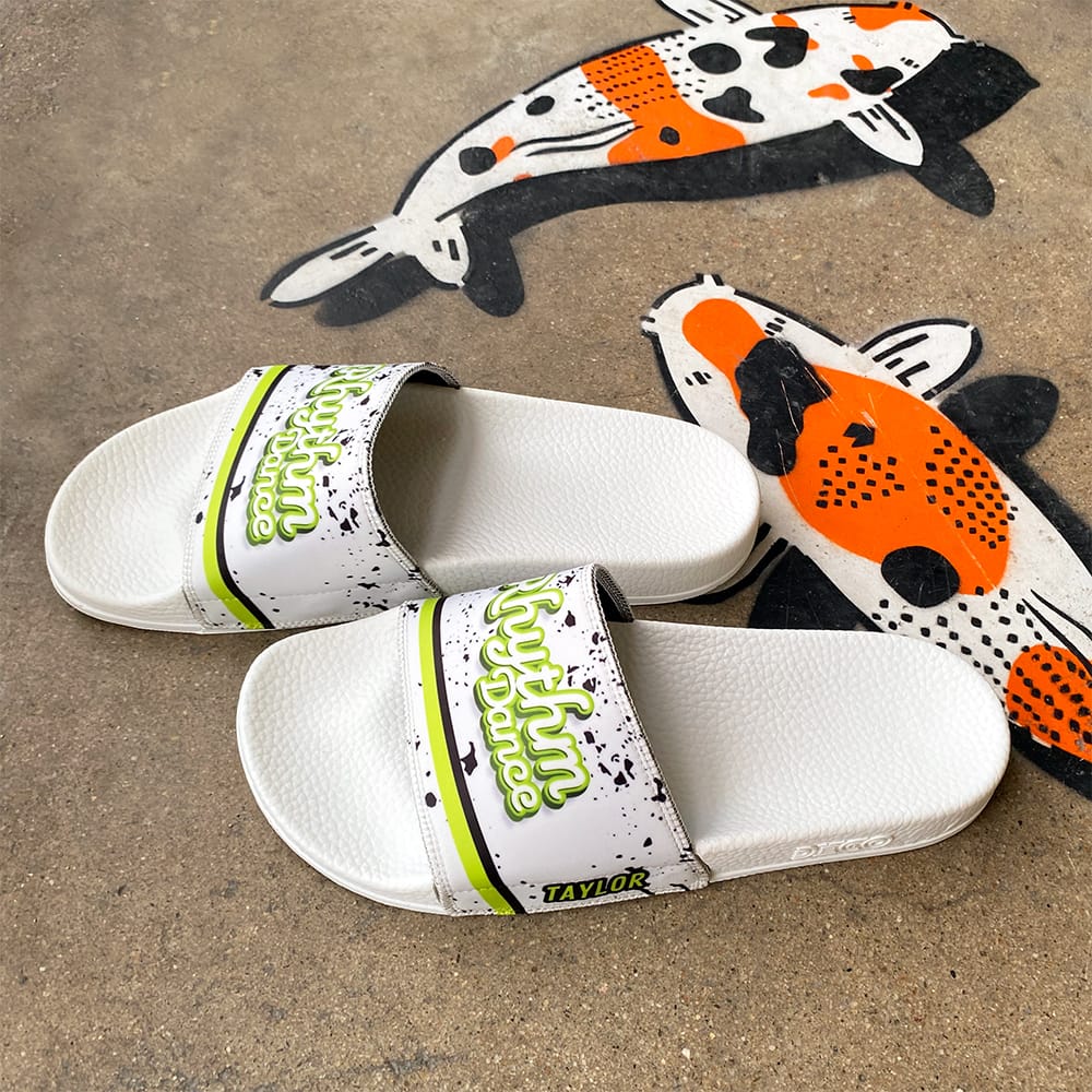 White custom dance-team slides with a green team logo and the name Taylor